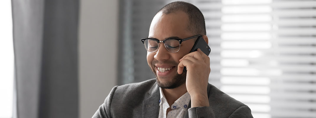 Lächelnder, brilletragender Vertriebsmitarbeiter führt ein Telefonat mit einem potentiellen Kunden.